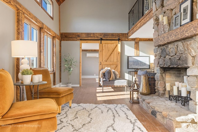 sitting room featuring a wall unit AC, a barn door, a towering ceiling, and hardwood / wood-style flooring