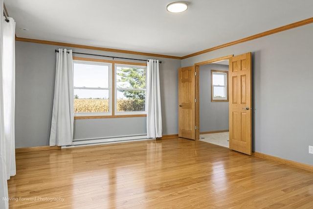 empty room featuring baseboard heating, light hardwood / wood-style flooring, and ornamental molding