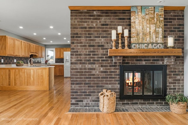 kitchen featuring sink, white fridge with ice dispenser, a brick fireplace, light hardwood / wood-style flooring, and backsplash