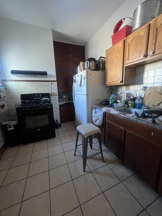 kitchen with backsplash, black range with gas cooktop, light tile patterned flooring, and white refrigerator