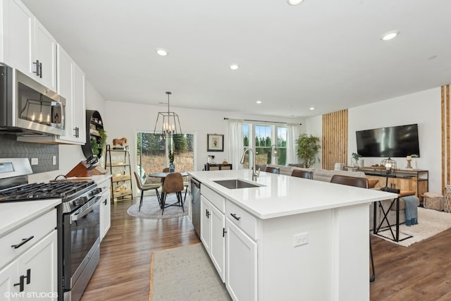 kitchen featuring white cabinets, sink, an island with sink, appliances with stainless steel finishes, and decorative light fixtures