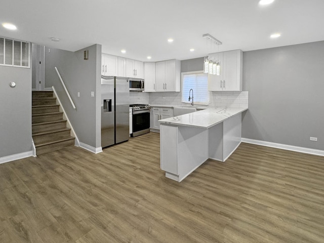 kitchen featuring pendant lighting, light hardwood / wood-style flooring, stainless steel appliances, white cabinets, and decorative backsplash