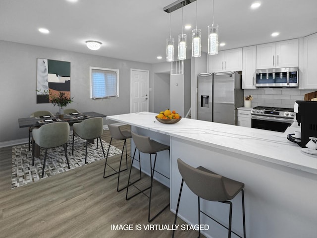 kitchen featuring appliances with stainless steel finishes, decorative light fixtures, white cabinetry, a kitchen bar, and light stone countertops