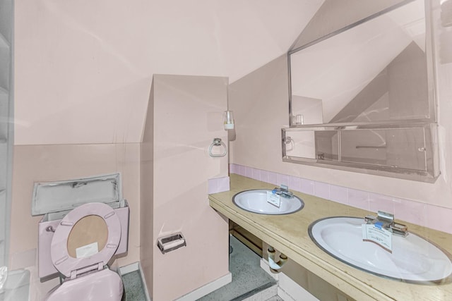 bathroom with double sink, vaulted ceiling, and toilet