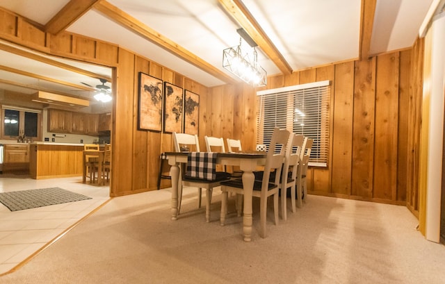 dining area with ceiling fan, beam ceiling, light colored carpet, and wooden walls