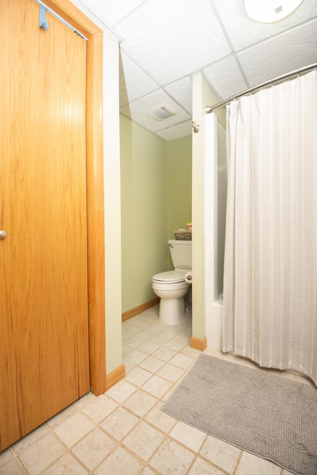 bathroom with shower / tub combo, toilet, and a drop ceiling