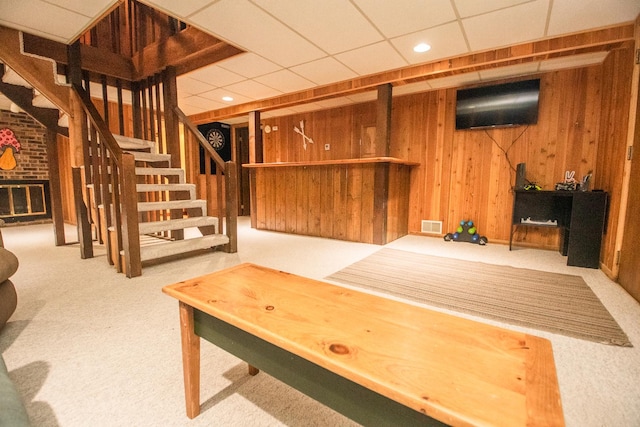 basement featuring light carpet, a fireplace, a drop ceiling, and wooden walls