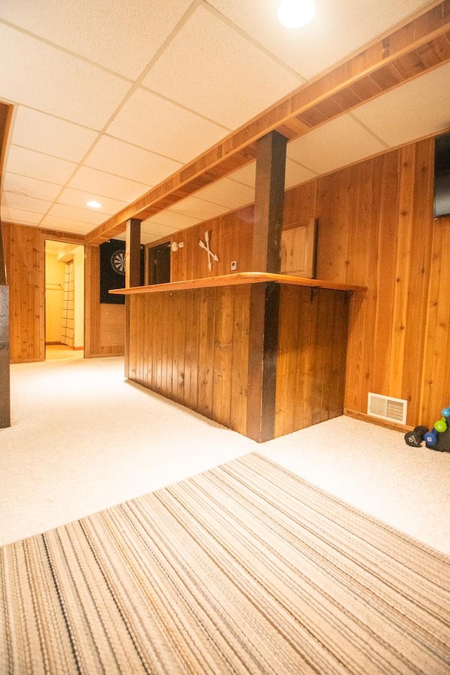 interior space featuring carpet, a drop ceiling, and wooden walls