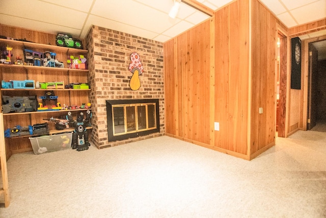 living room with light colored carpet, a brick fireplace, a drop ceiling, and wood walls