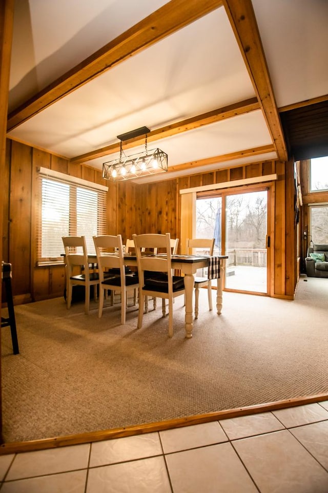 carpeted dining room featuring beam ceiling, a healthy amount of sunlight, and wood walls