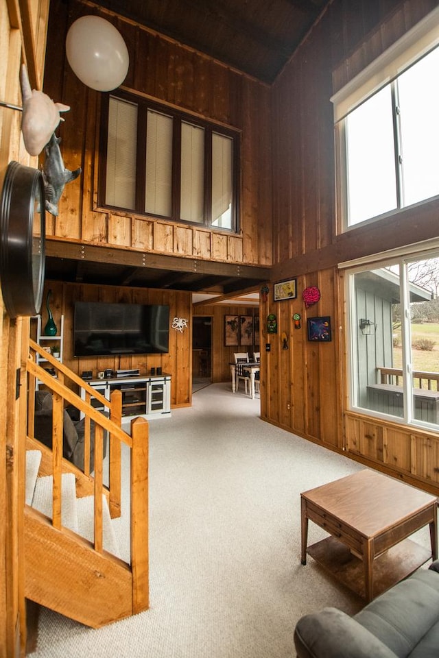 carpeted living room featuring a towering ceiling and wood walls