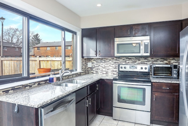 kitchen with backsplash, sink, light tile patterned floors, appliances with stainless steel finishes, and light stone counters