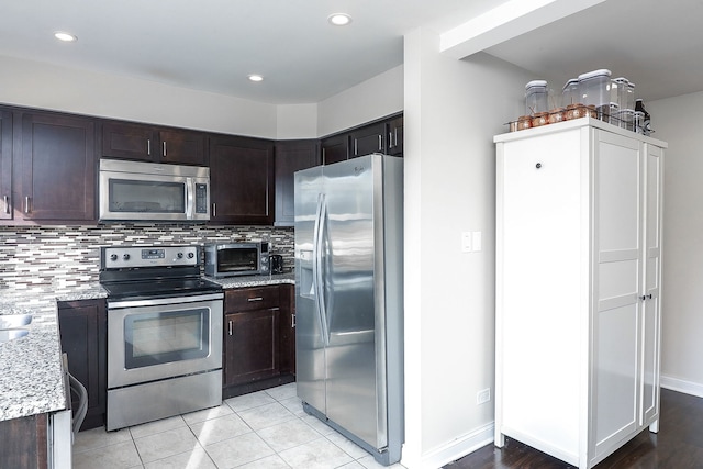 kitchen with appliances with stainless steel finishes, tasteful backsplash, light stone counters, dark brown cabinets, and light tile patterned flooring