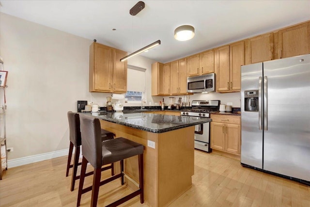 kitchen with a breakfast bar area, decorative light fixtures, light wood-type flooring, dark stone countertops, and appliances with stainless steel finishes