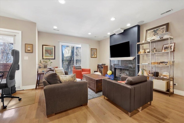 living room with a high end fireplace and light hardwood / wood-style flooring