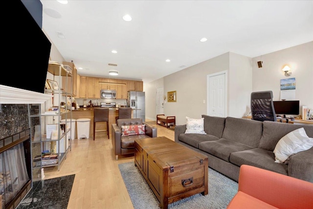 living room with a high end fireplace and light hardwood / wood-style floors