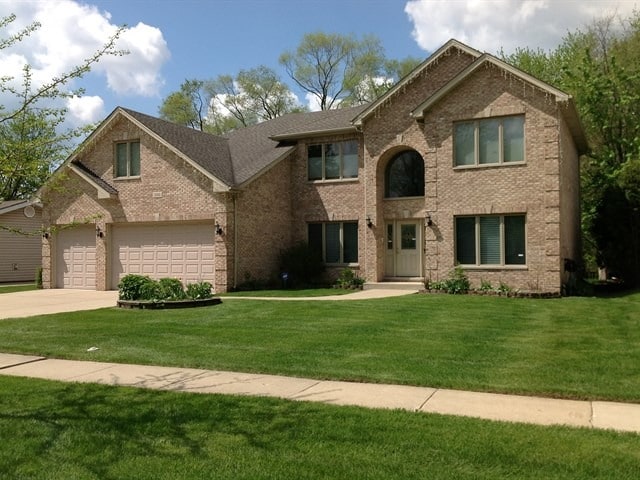 view of front of home with brick siding, driveway, and a front lawn