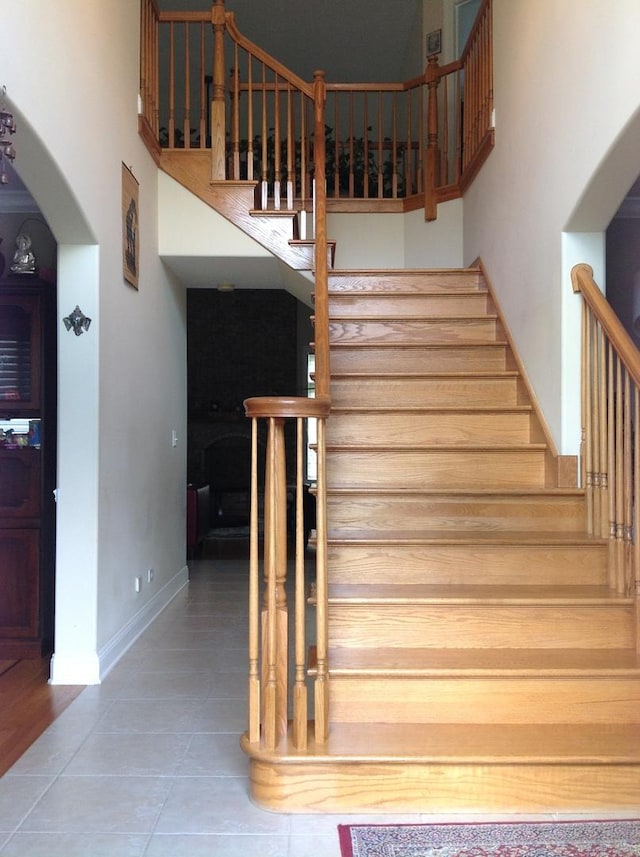 stairway featuring tile patterned floors, a high ceiling, arched walkways, and baseboards