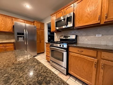 kitchen featuring backsplash, light tile patterned floors, stainless steel appliances, and dark stone counters