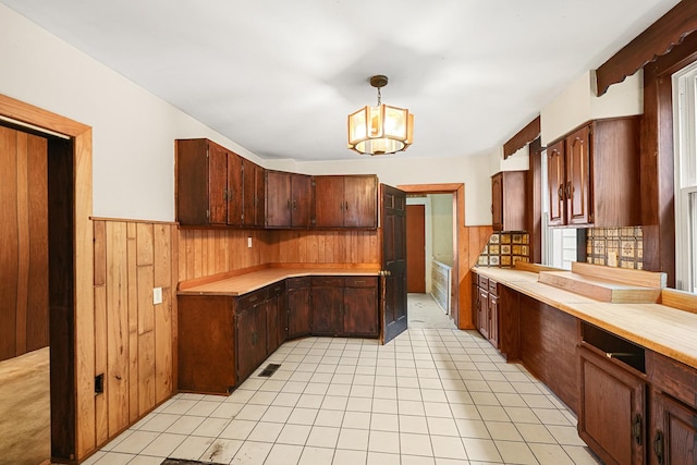 kitchen featuring dark brown cabinets, wood walls, a notable chandelier, and pendant lighting