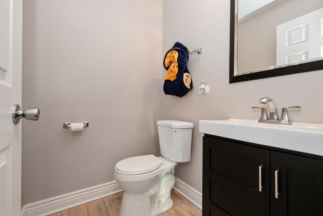 half bath featuring baseboards, toilet, wood finished floors, and vanity