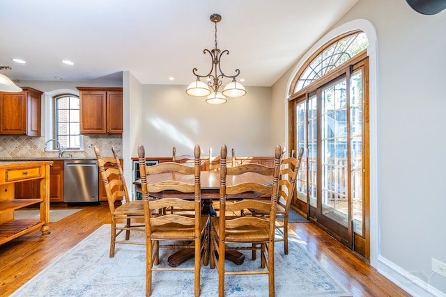 dining space featuring sink, plenty of natural light, light wood-type flooring, and an inviting chandelier