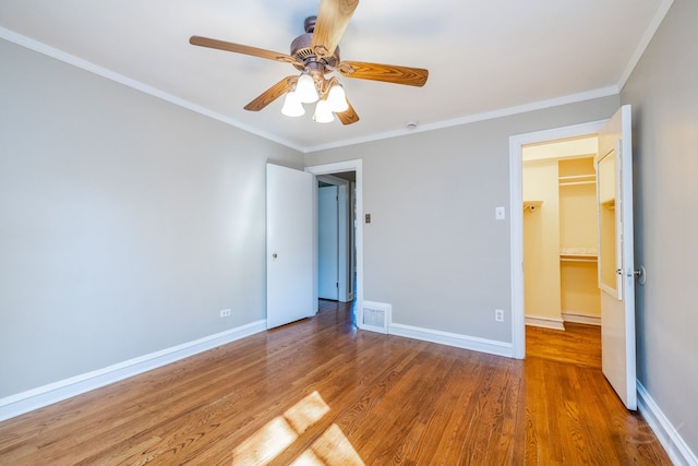 unfurnished bedroom featuring a walk in closet, ornamental molding, ceiling fan, wood-type flooring, and a closet