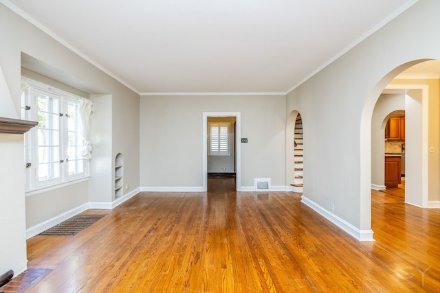 empty room featuring built in shelves, wood-type flooring, and ornamental molding