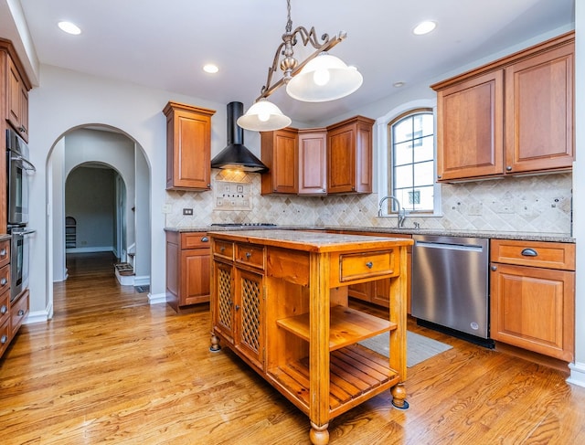 kitchen with wall chimney exhaust hood, a kitchen island, stainless steel dishwasher, decorative light fixtures, and double wall oven