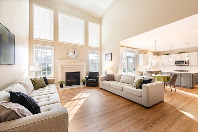 living room featuring light hardwood / wood-style floors, plenty of natural light, a towering ceiling, and a tiled fireplace