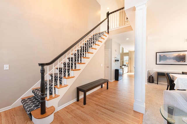 staircase with wood-type flooring, a towering ceiling, and ornate columns