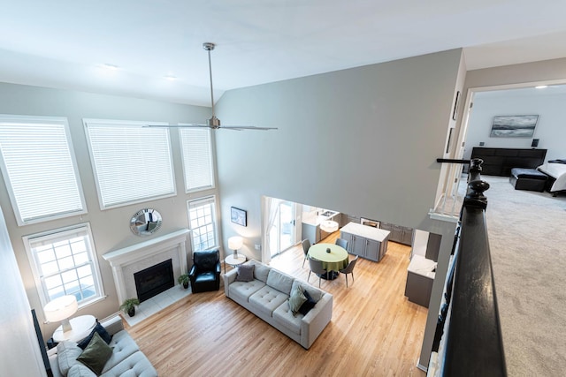 living room featuring ceiling fan, light hardwood / wood-style flooring, high vaulted ceiling, and a fireplace