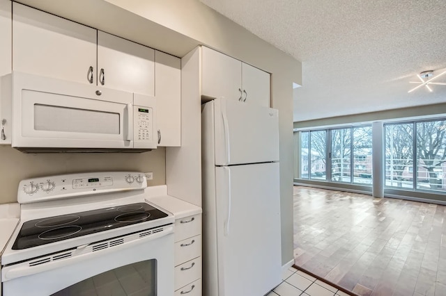 kitchen featuring white appliances, plenty of natural light, a textured ceiling, and white cabinets