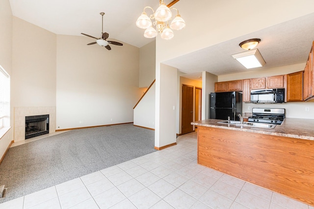 kitchen with black appliances, ceiling fan with notable chandelier, light tile patterned floors, kitchen peninsula, and a tiled fireplace