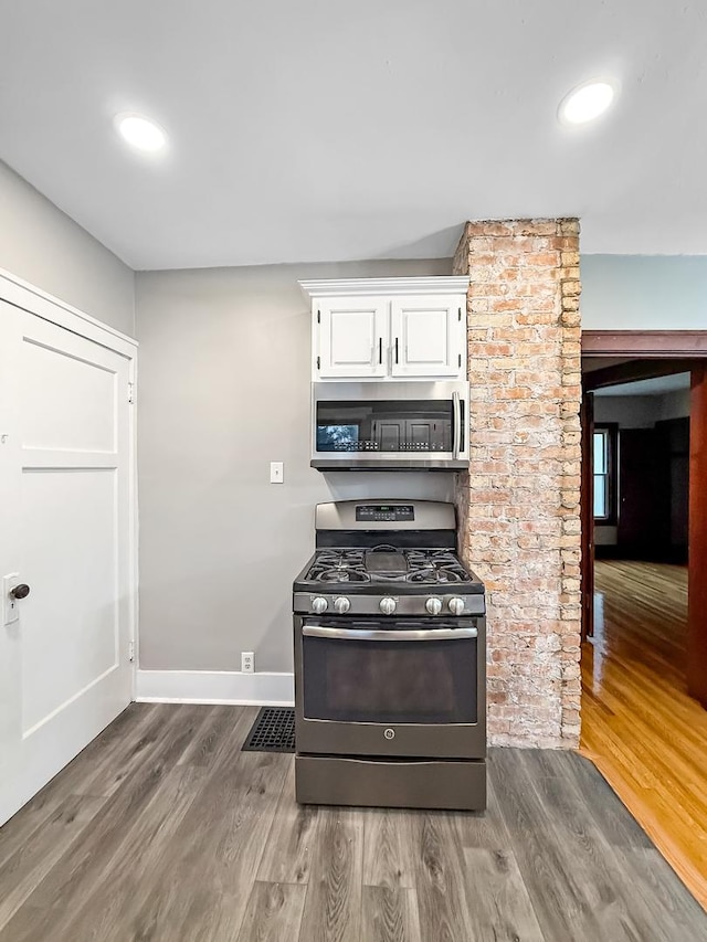 kitchen with appliances with stainless steel finishes, white cabinetry, and hardwood / wood-style floors