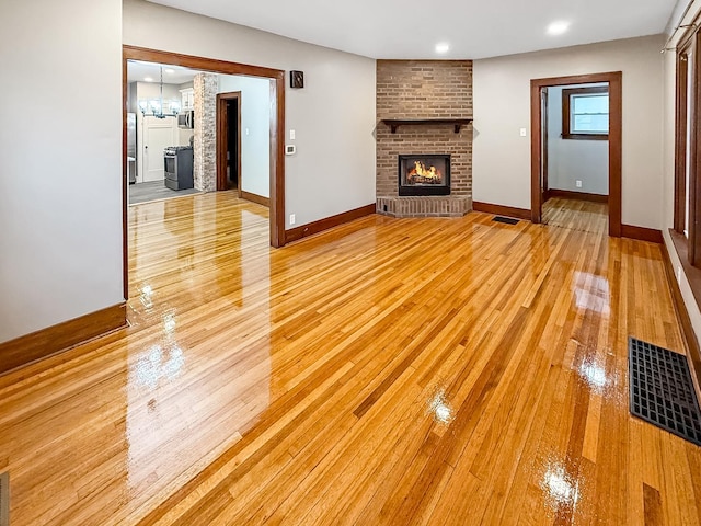 unfurnished living room with light hardwood / wood-style flooring, a brick fireplace, and a notable chandelier