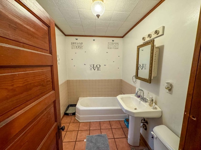 bathroom featuring tile patterned floors, ornamental molding, tile walls, toilet, and a bathing tub