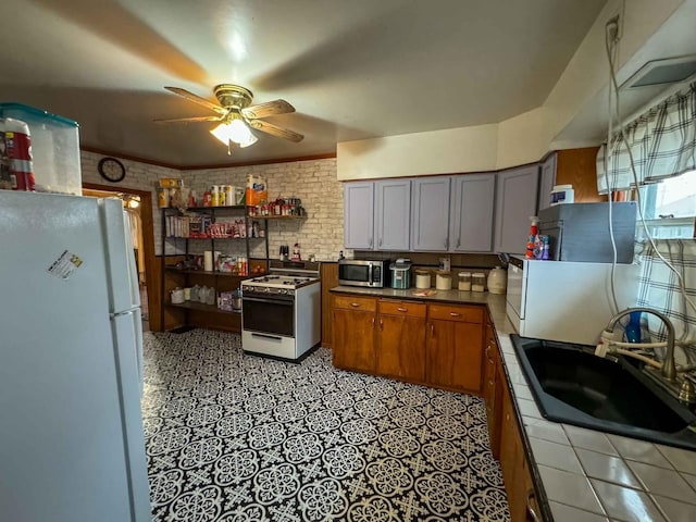 kitchen with ceiling fan, tile counters, sink, brick wall, and white appliances