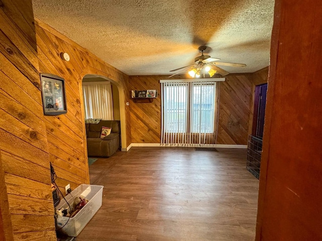 interior space featuring a textured ceiling, ceiling fan, wood walls, and dark wood-type flooring