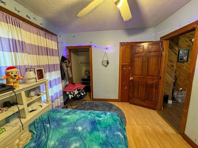 bedroom featuring a textured ceiling, light hardwood / wood-style flooring, ceiling fan, and wood walls