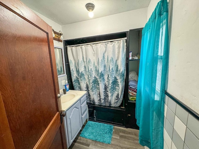 bathroom with hardwood / wood-style flooring, vanity, shower / bath combination with curtain, and tile walls