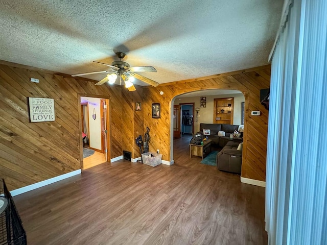 living room with ceiling fan, wood walls, wood-type flooring, and a textured ceiling