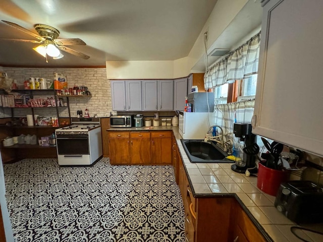 kitchen with tile countertops, sink, ceiling fan, white range with gas cooktop, and brick wall