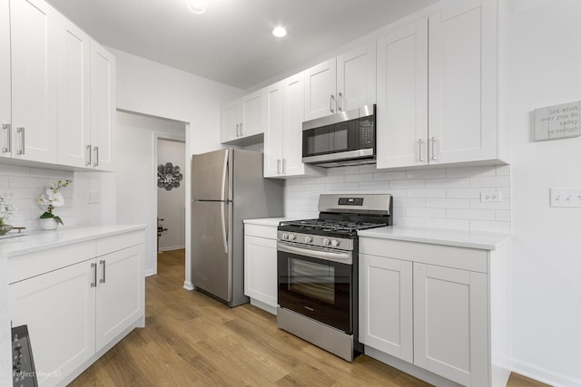 kitchen featuring decorative backsplash, light stone countertops, stainless steel appliances, white cabinets, and light hardwood / wood-style floors