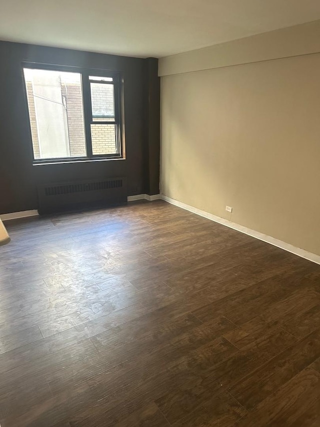 spare room featuring dark wood-type flooring and radiator heating unit