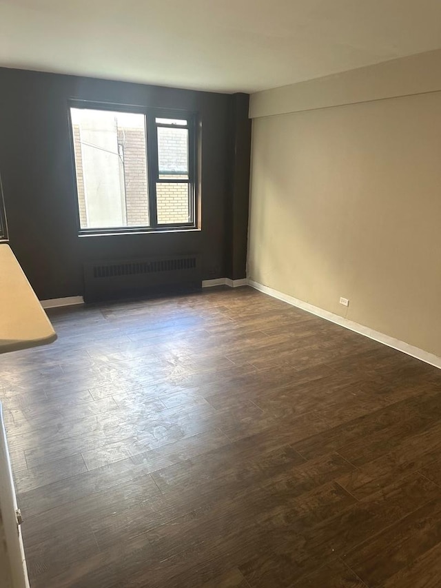 spare room with dark hardwood / wood-style flooring and radiator heating unit