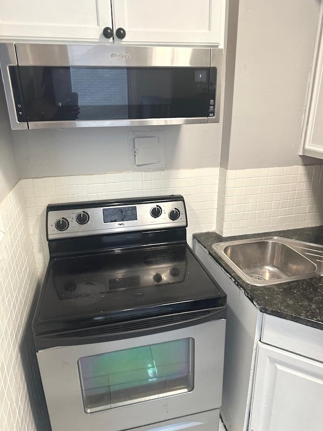 kitchen featuring backsplash, dark stone countertops, sink, white cabinetry, and appliances with stainless steel finishes