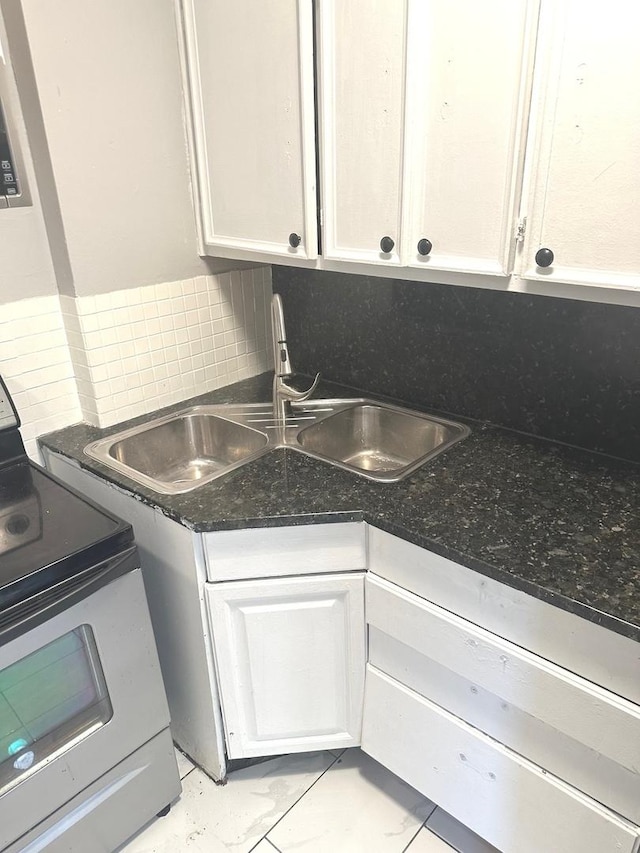 kitchen featuring electric stove, decorative backsplash, sink, white cabinets, and dark stone counters