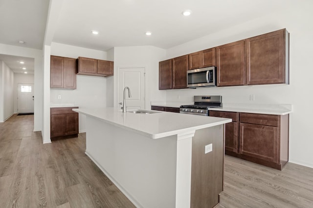 kitchen with an island with sink, appliances with stainless steel finishes, sink, and light wood-type flooring