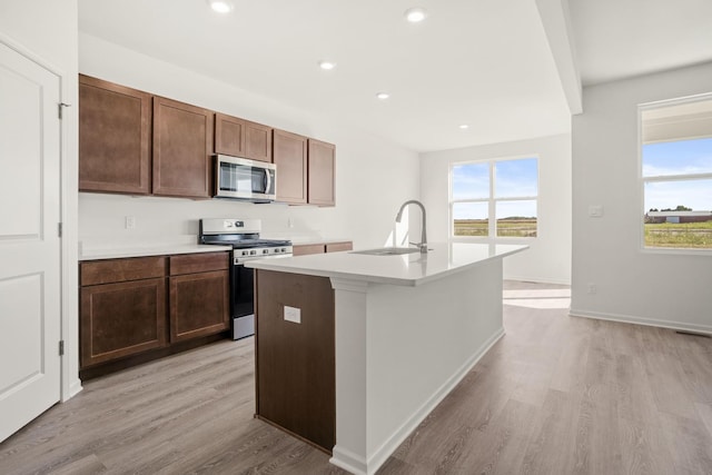 kitchen featuring sink, a kitchen island with sink, dark brown cabinetry, stainless steel appliances, and light hardwood / wood-style flooring